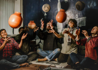 Five people are sitting in a semi-circle formation, they are each throwing a ceramic vessel into the air.