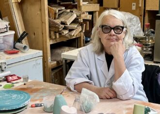 Caroline Gray sits at a table with a collection of her work, brightly coloured ceramic pillars and spheres.